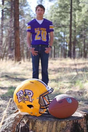 Blue Ridge football helmet and ball on tree stump with player wearing number 20 jersey in background.