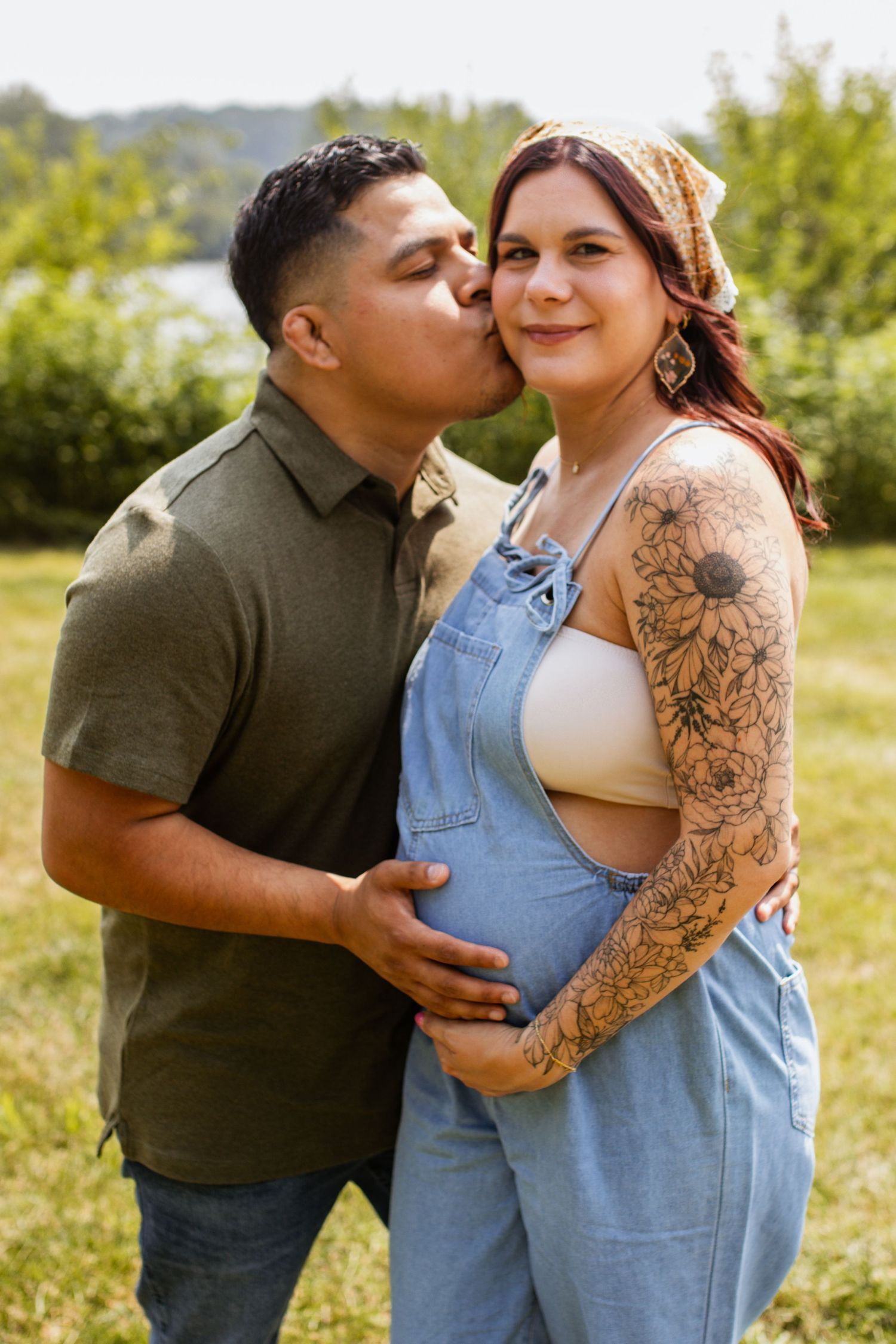 Romantic couple sharing tender moments in a sunny field with one wearing denim overalls.