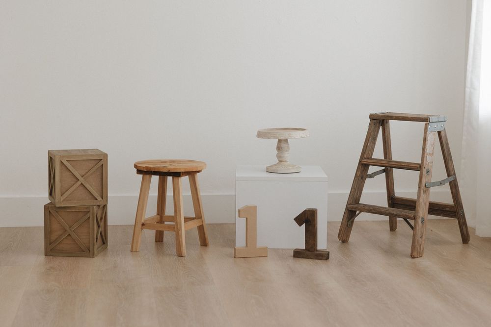 Rustic wooden decor set with crate, round stool, pedestal, number one sign, and step ladder on light wood floor.
