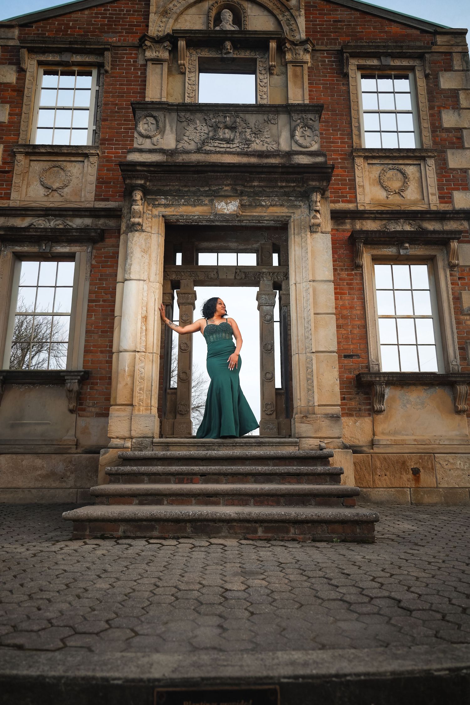 Woman in emerald green gown posing at historic brick building entrance.