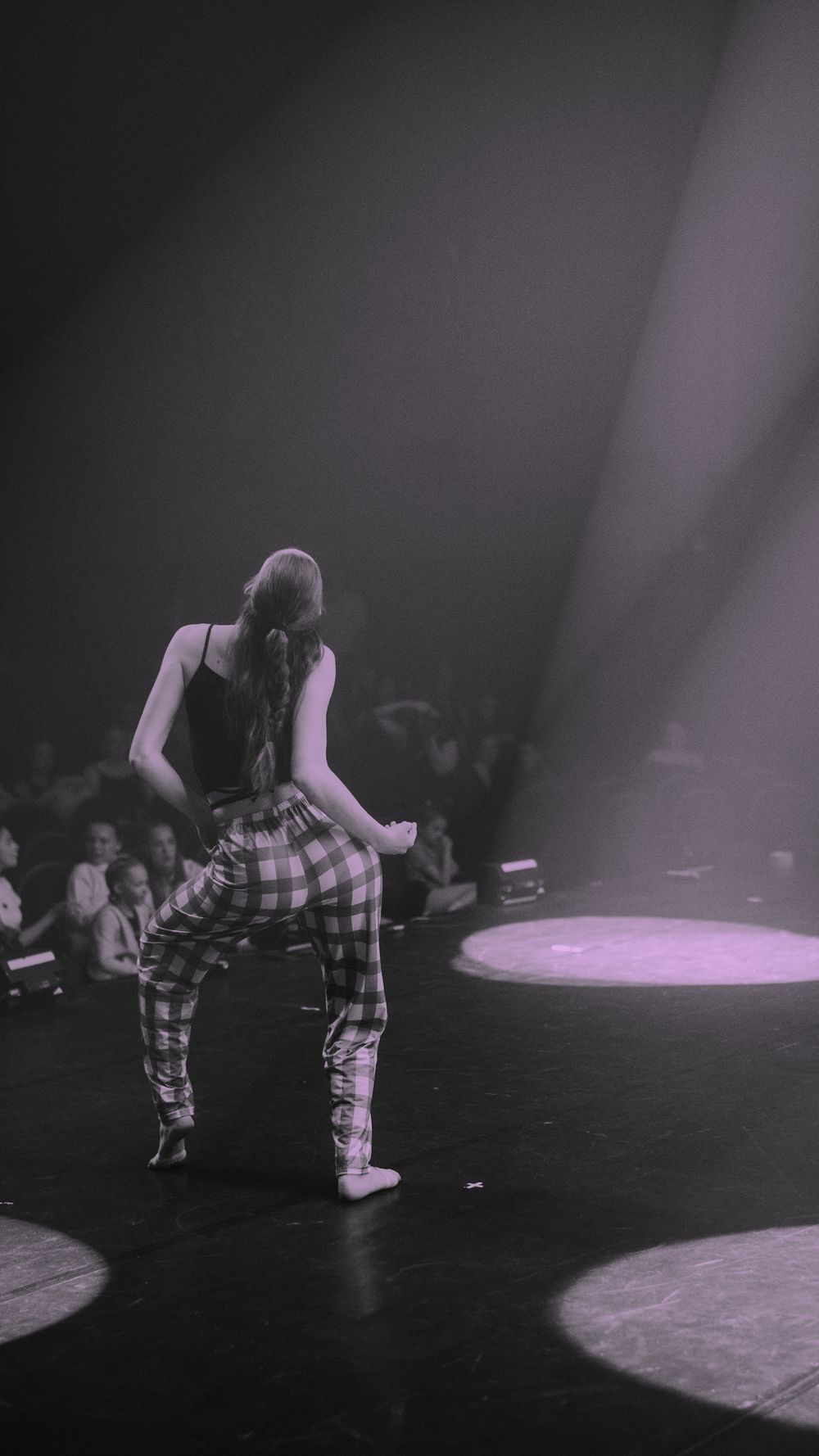 Concert performer on stage wearing plaid pants seen in dramatic black and white lighting with spotlights on dark floor.