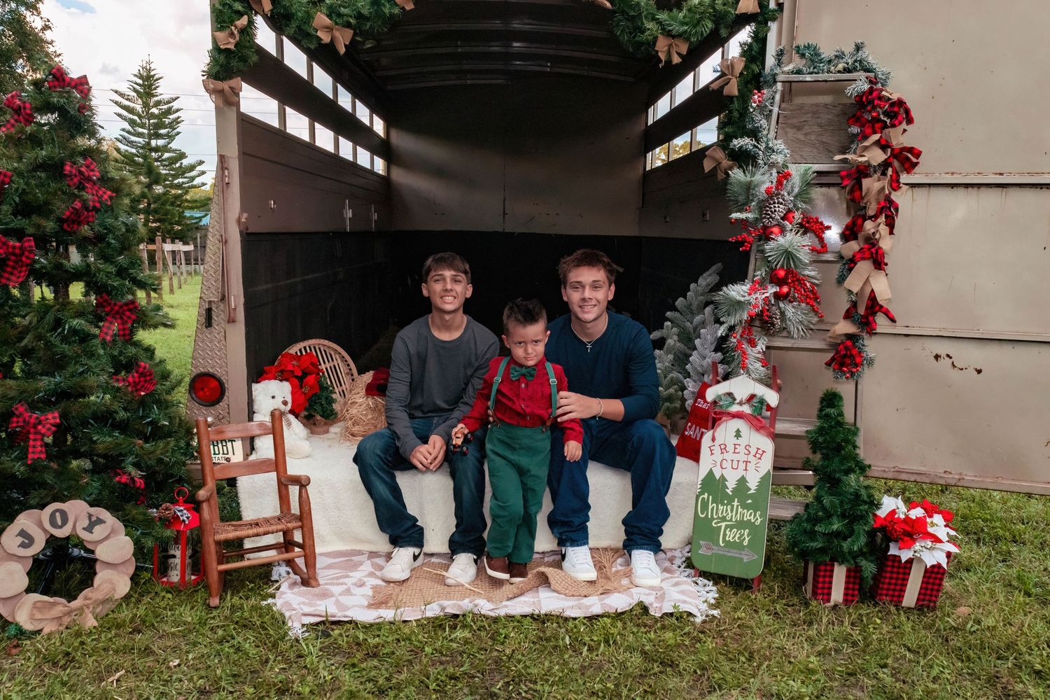 Outdoor Christmas family portraits with decorated trees and rustic barn setting.