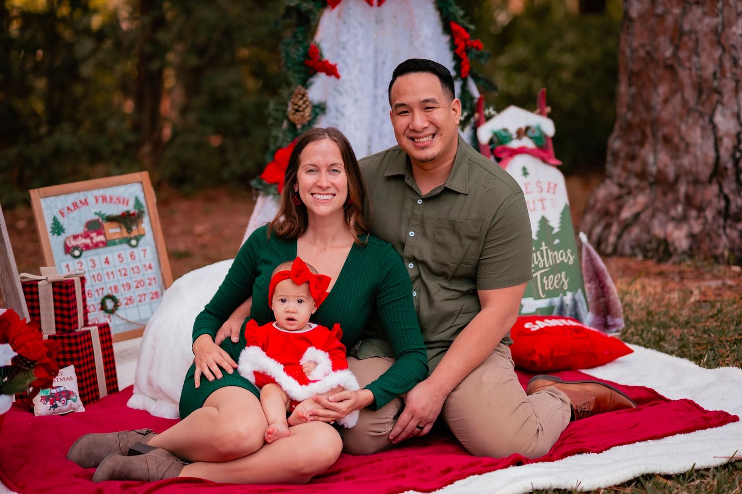 Holiday family photos on red blanket with Christmas decorations and pine trees in background.