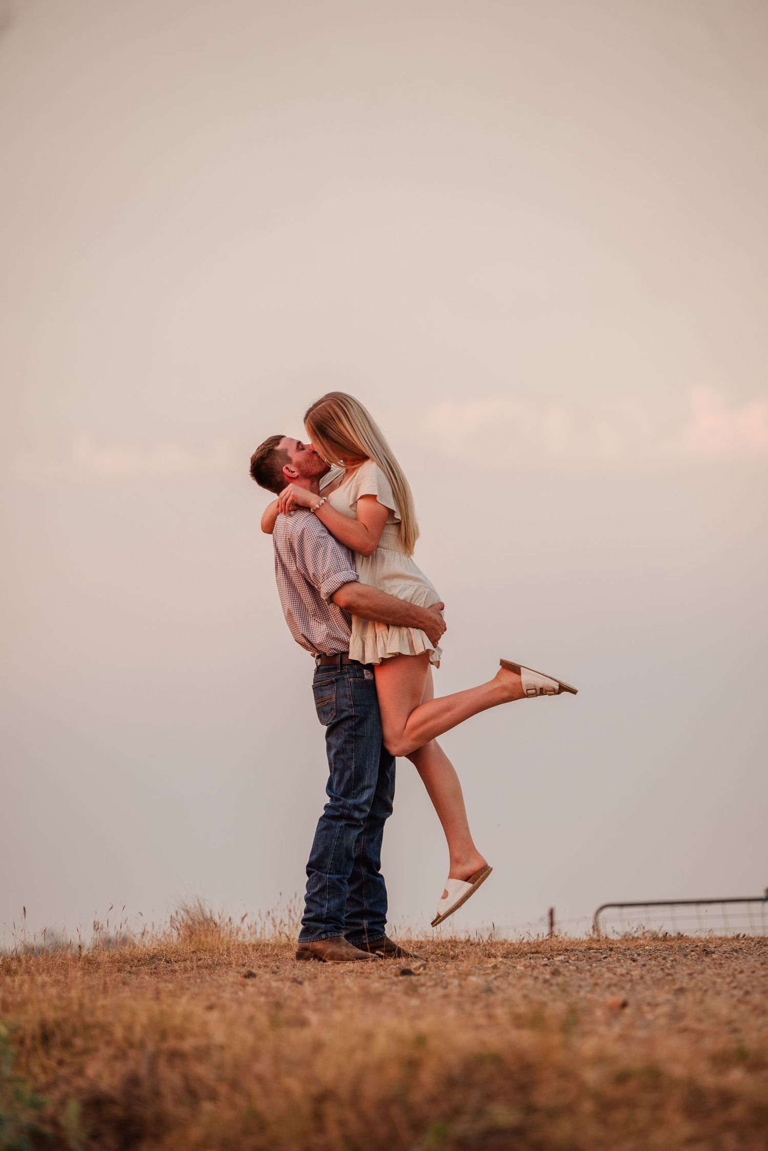 A romantic couple embraces in a sun-drenched field during golden hour.