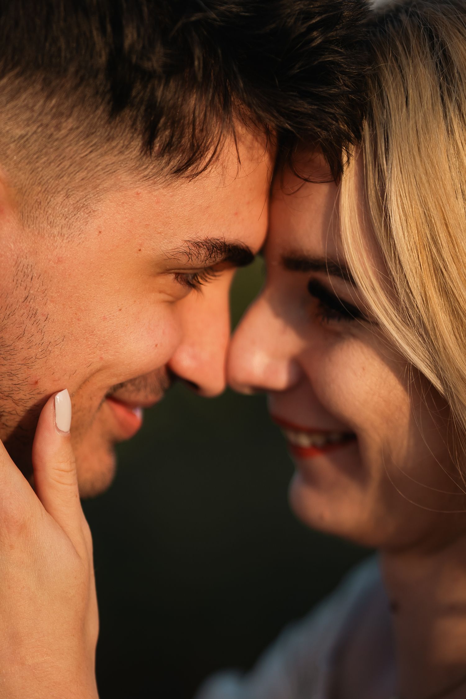 Close up romantic portrait of a couple touching foreheads and smiling tenderly in warm lighting.