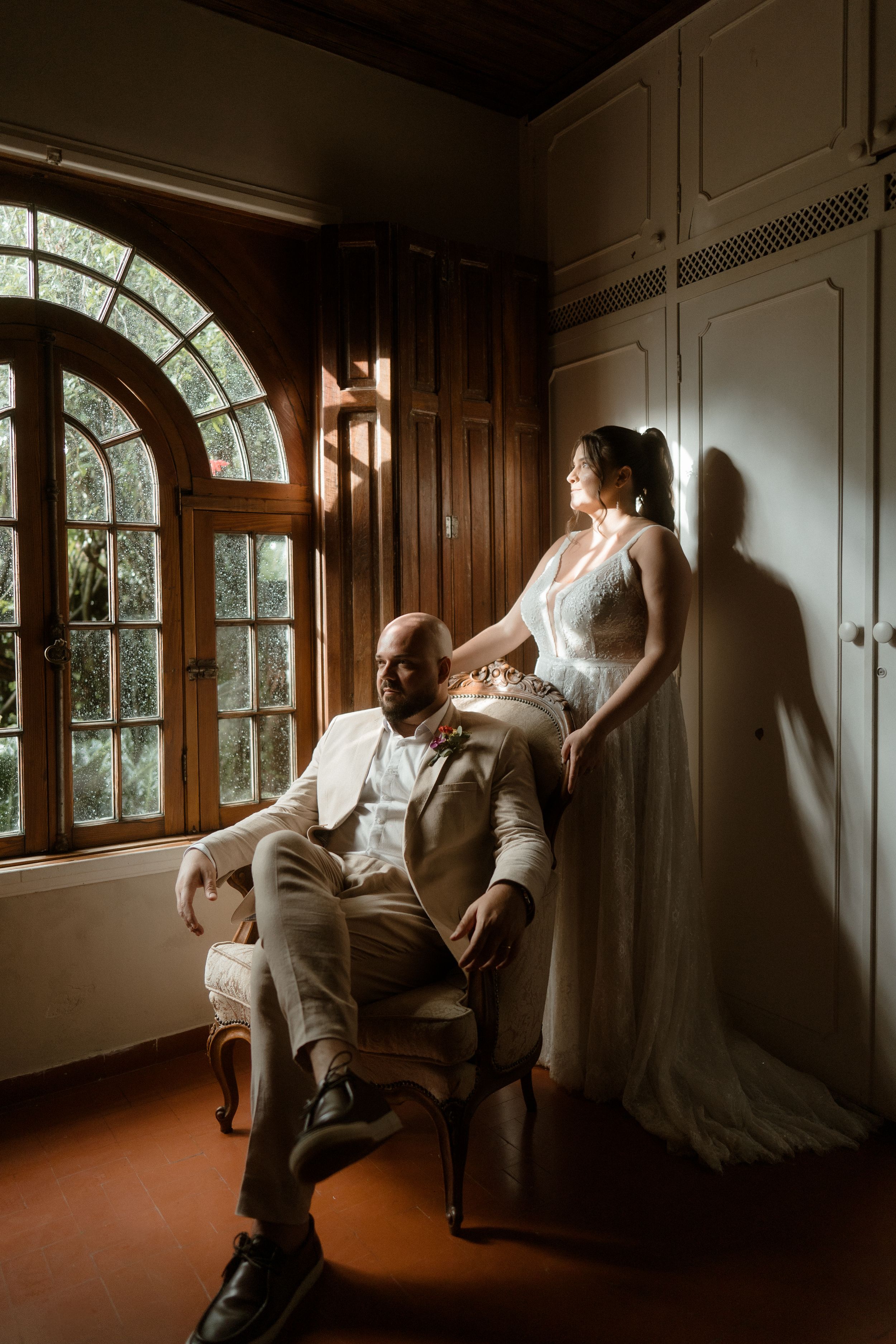Artistic wedding portrait in a wood-paneled room with arched windows and dramatic lighting.