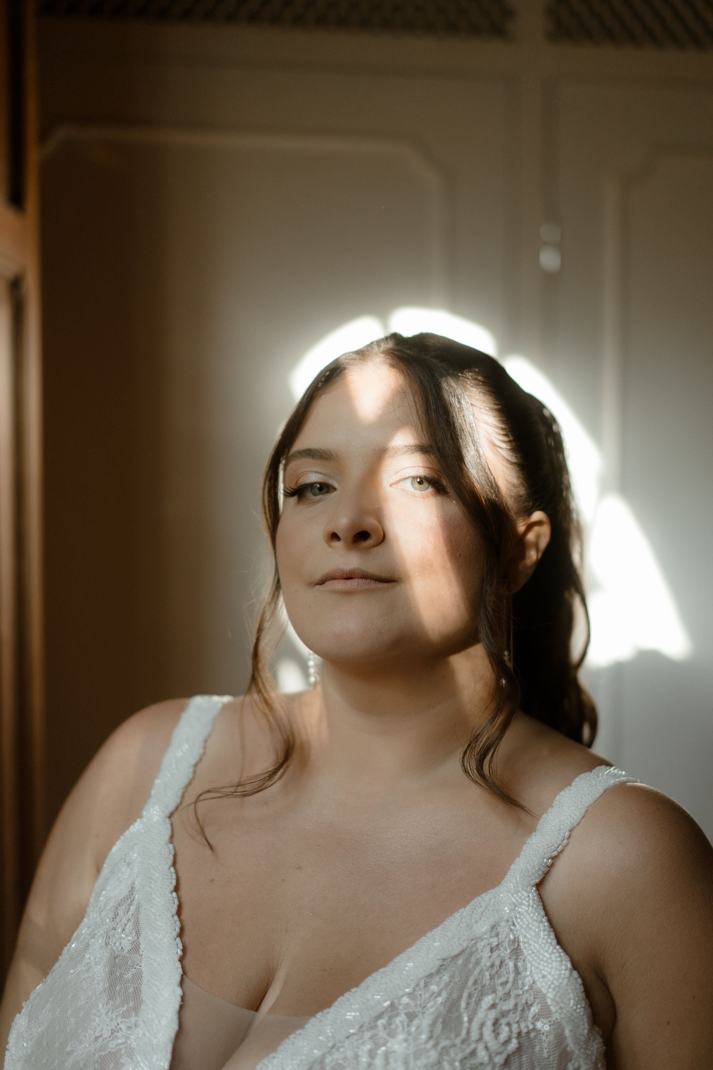 Backlit bridal portrait with glowing halo effect against neutral wall background.