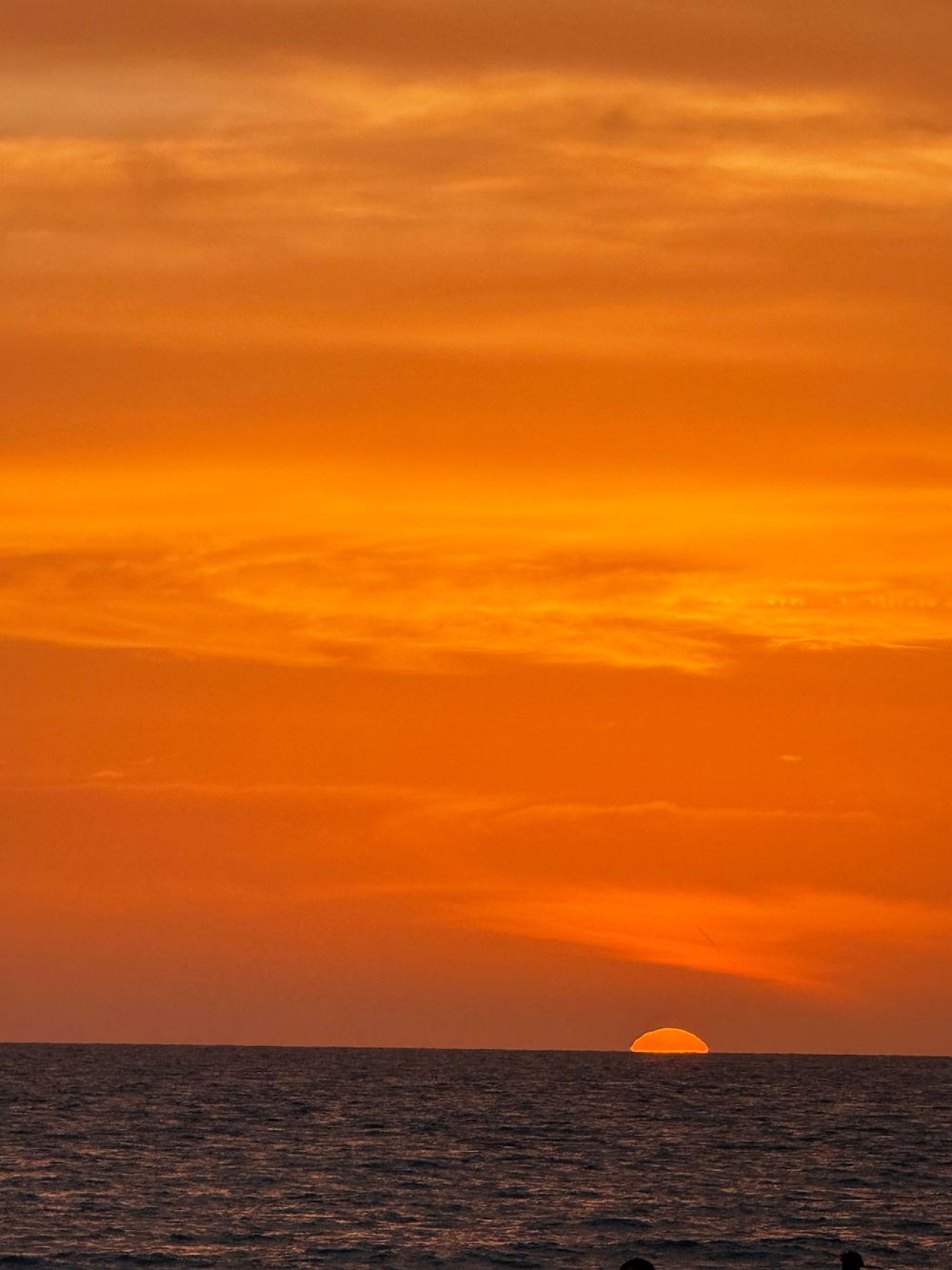 A vibrant orange sunset over dark ocean waters with the sun barely visible on the horizon.