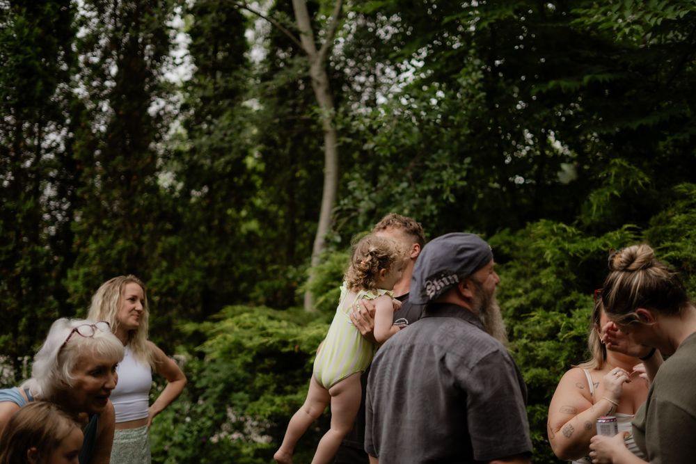 Group of people gathered outdoors surrounded by lush green trees during an event.