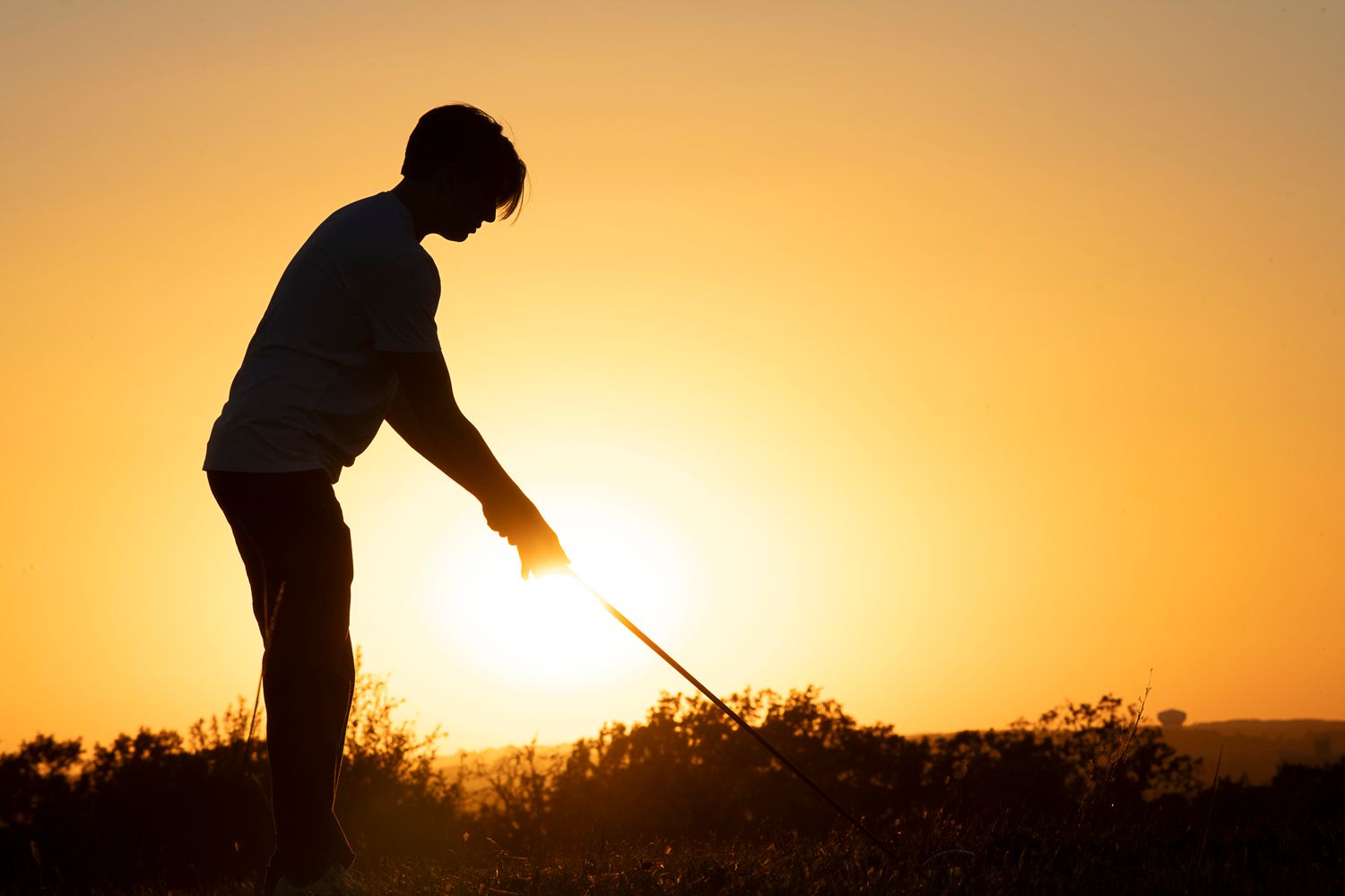 Silhouette of a person golfing at sunset with a warm orange sky in the background.