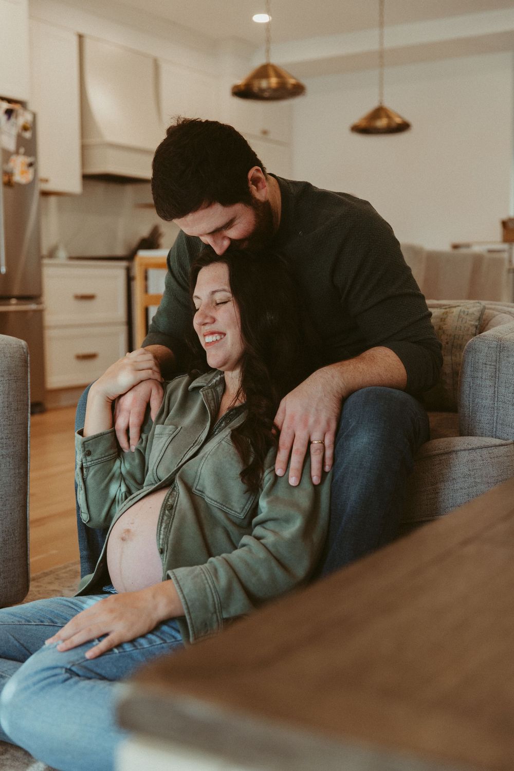 Intimate maternity moment showing couple relaxing together on couch in modern living room.