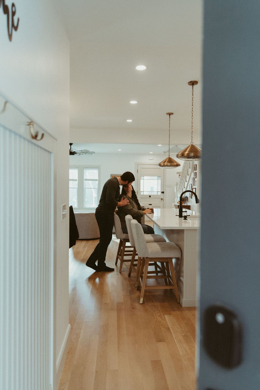 A couple shares an intimate moment in a bright modern kitchen with pendant lights and hardwood floors.