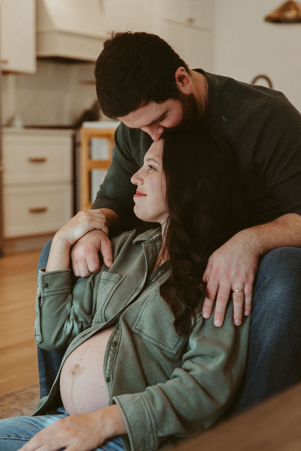 Tender pregnancy moment captured between couple on comfortable couch.