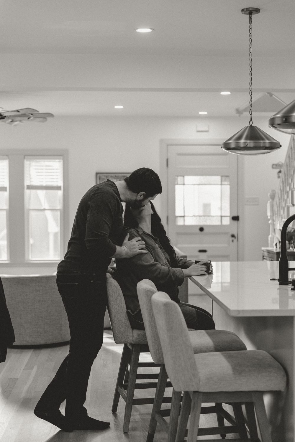 Black and white photo of a romantic moment between two people in a contemporary kitchen setting.