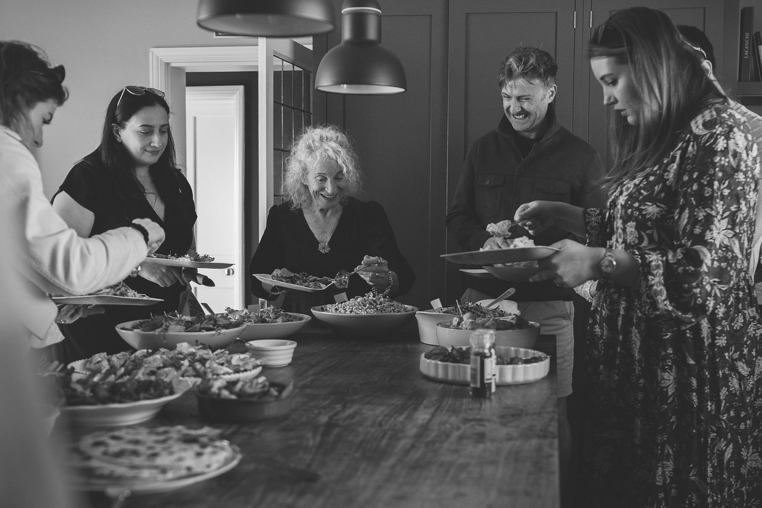 A group of people gather around a rustic wooden table to share a meal together in black and white.