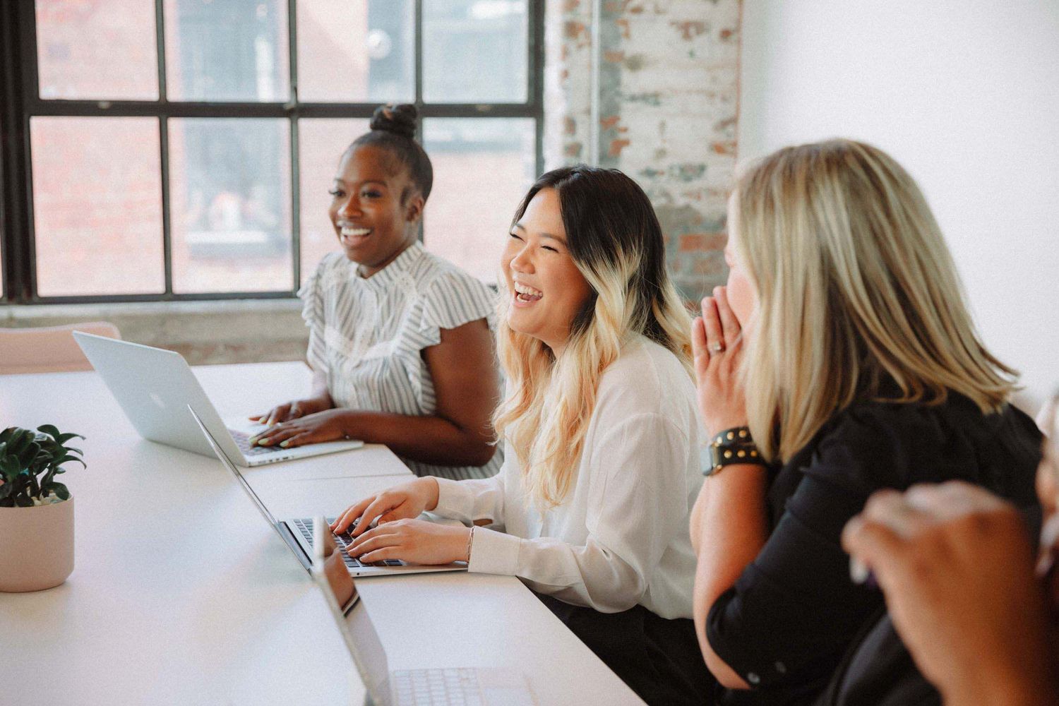 Group of diverse professionals collaborating at a conference table with laptops in a bright modern office space.