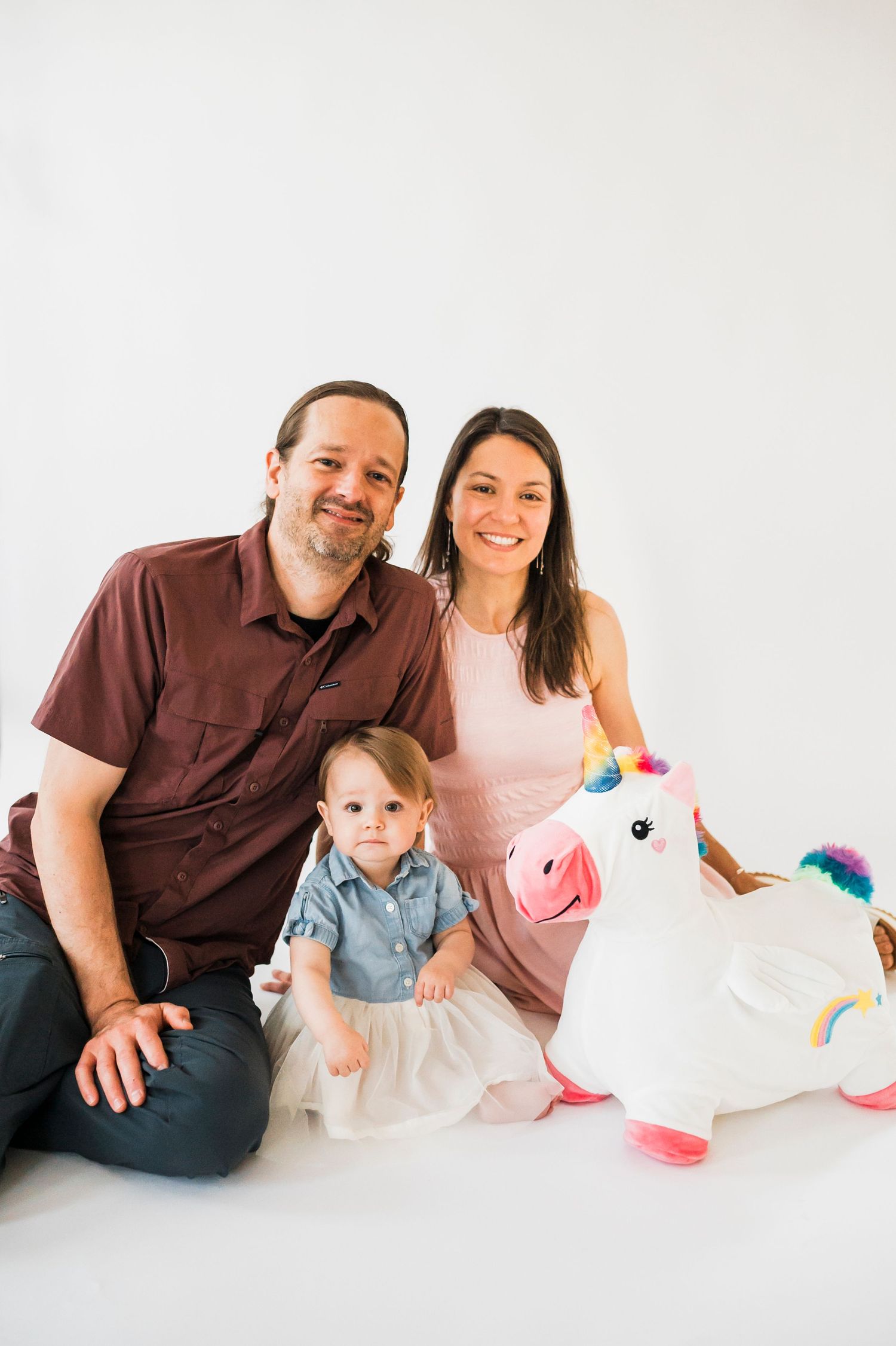 Studio family portrait with young child and inflatable unicorn toy on white background.