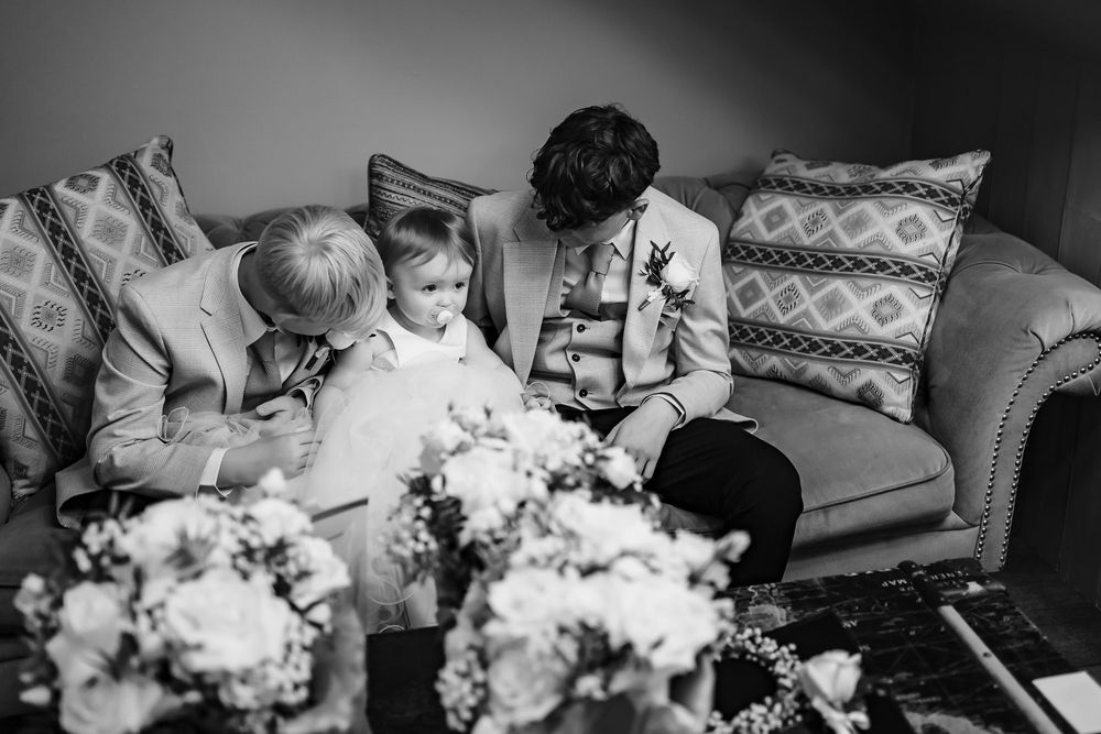 Black and white candid moment of family sitting together on couch with young child and bouquet of flowers in foreground.