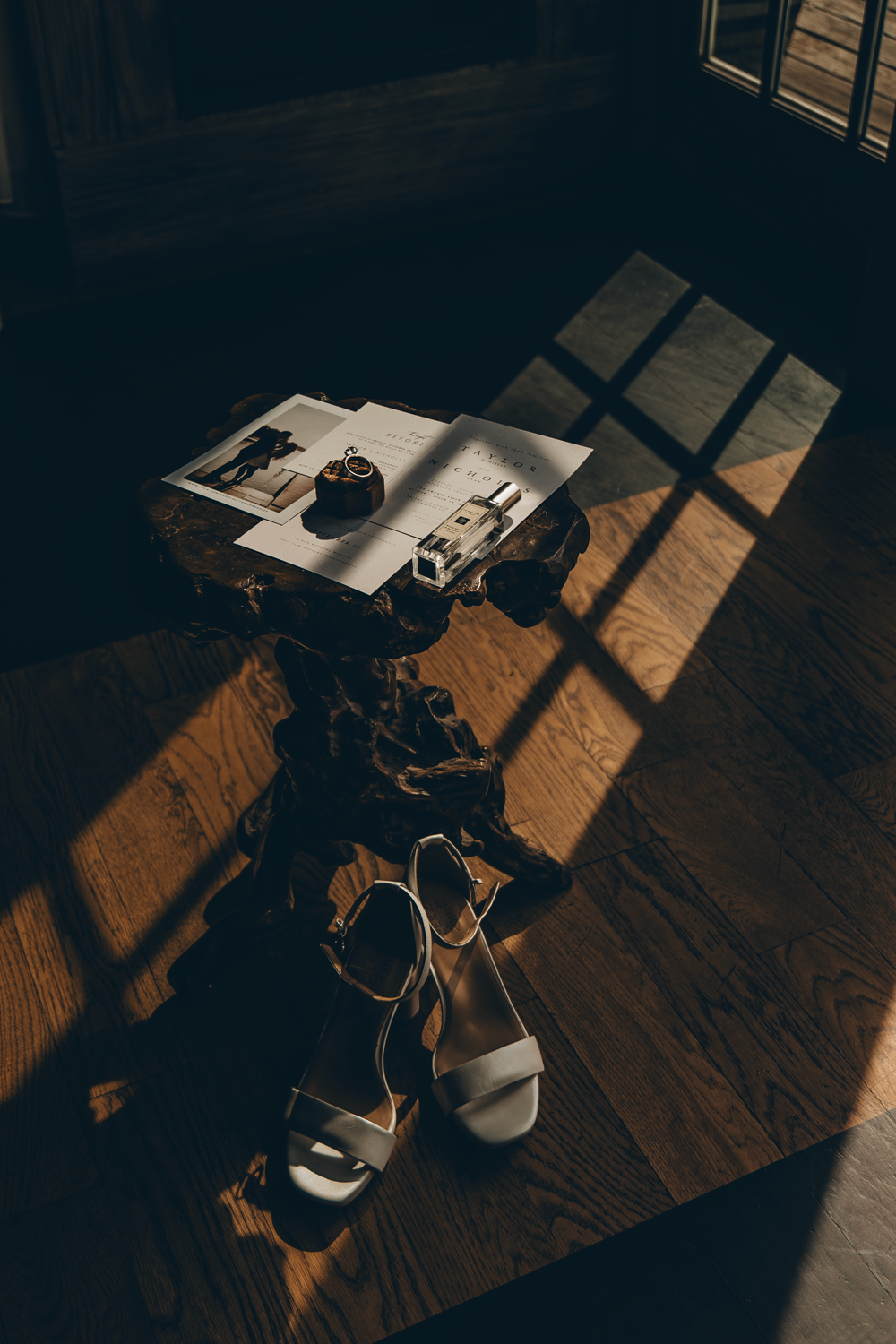 A high-angle view of photographs and sandals on a wooden floor with dramatic window light casting shadows.