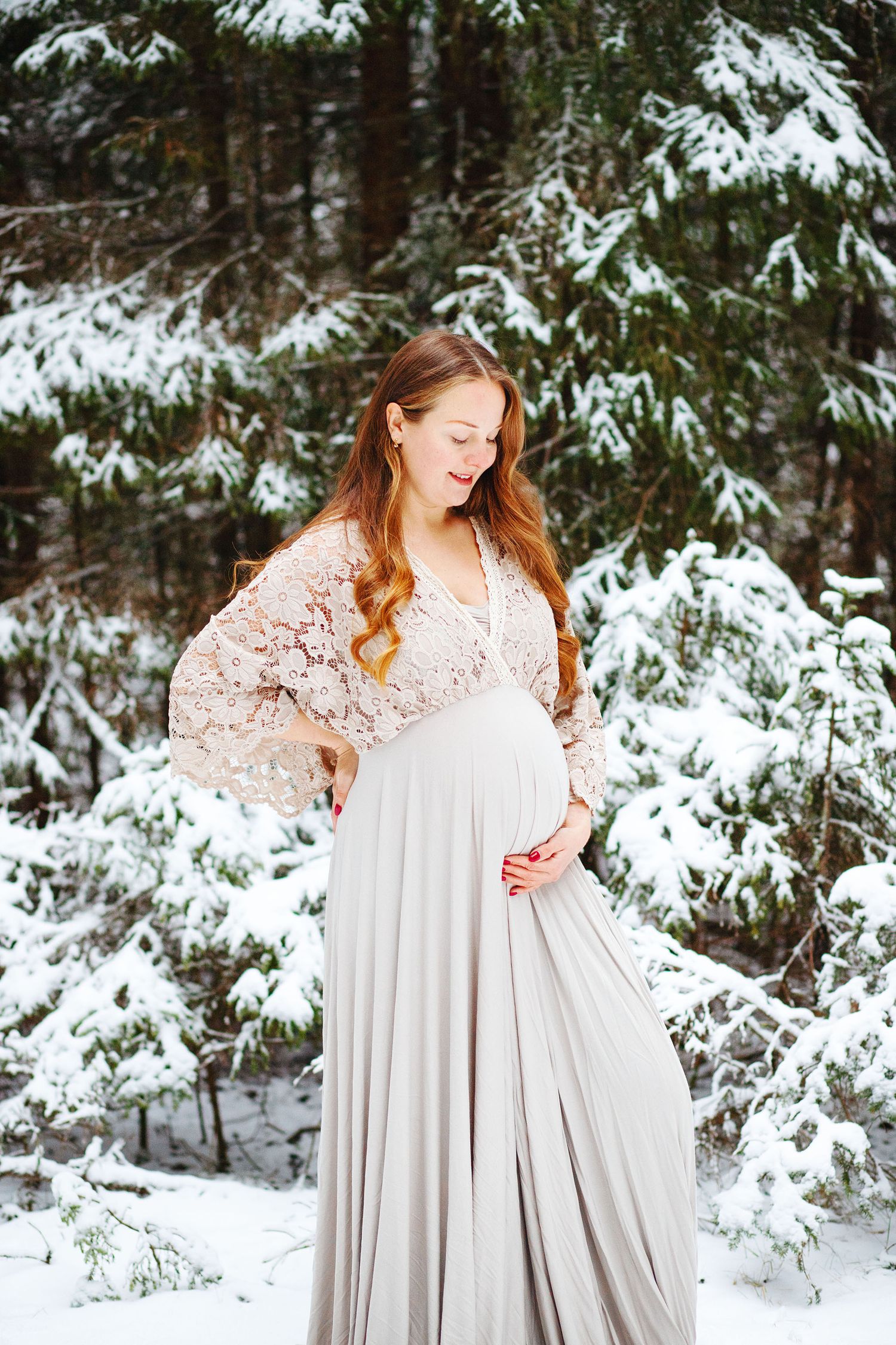 Gravid tjej som står och håller sig om magen i ett vinterlandskap. Gravidfotografering Härnösand. BF december. Höga kusten. Graviditet.