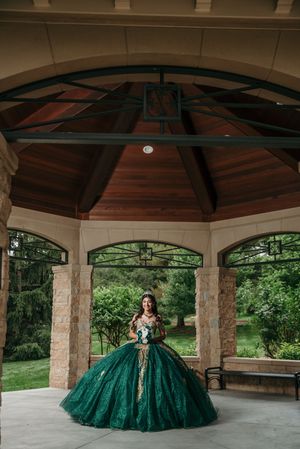 Dramatic emerald ball gown displayed in covered stone pavilion with wooden ceiling.