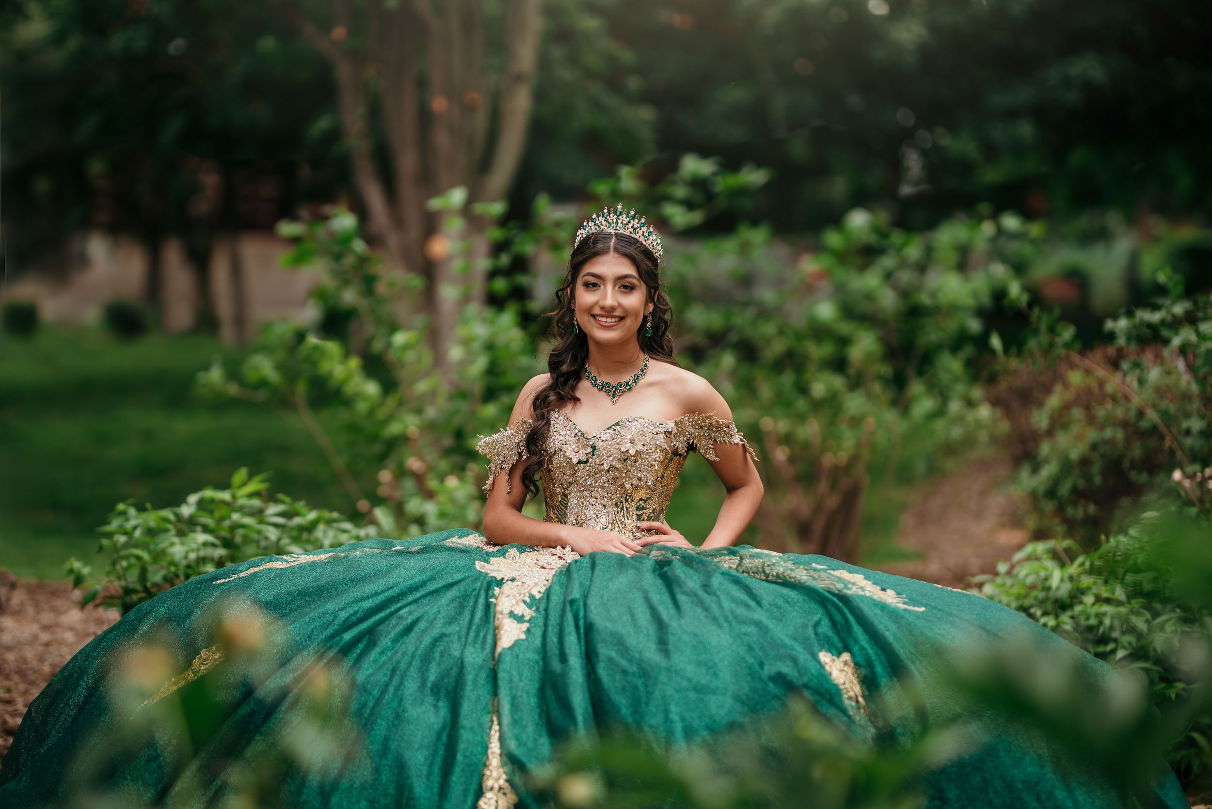 Emerald green ball gown photographed in lush garden setting.