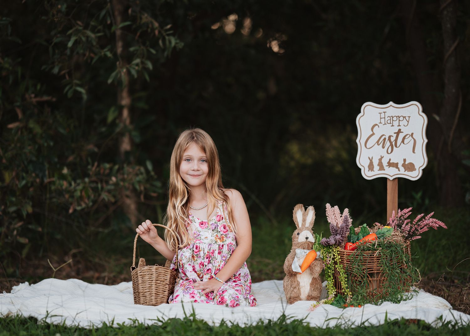 Easter holiday setup with decorative bunnies and greenery on white blanket outdoors.