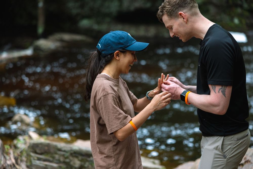 Couple examining a small creature by a rocky river during an outdoor nature adventure.