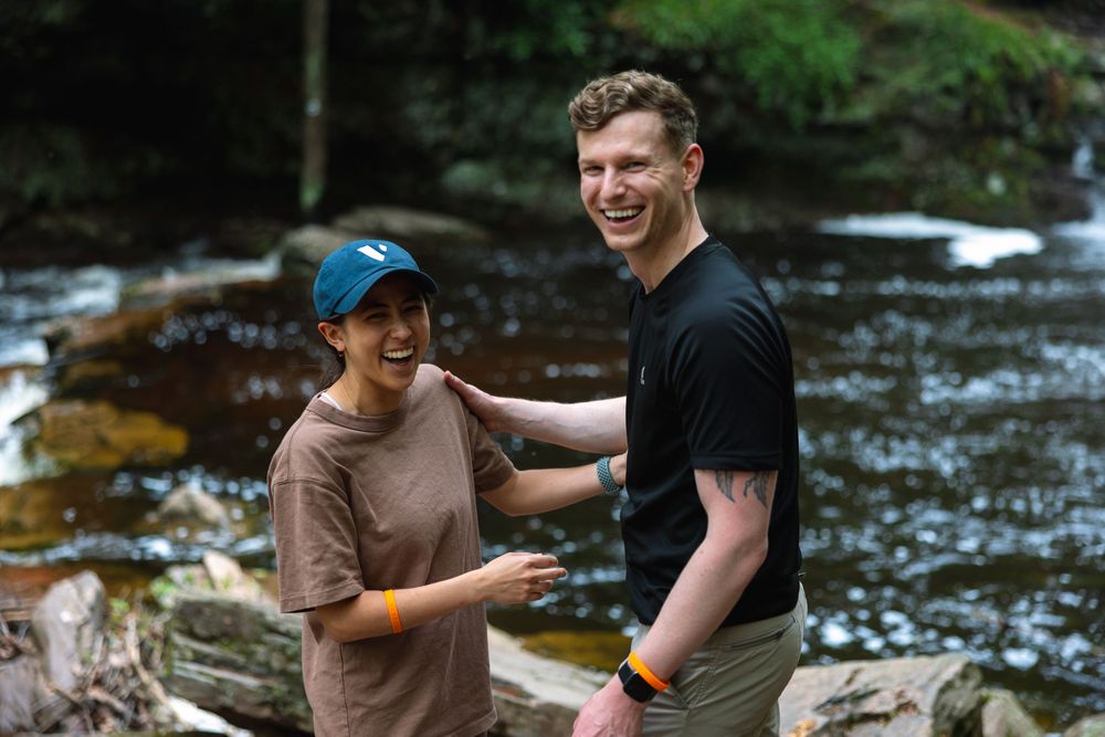 Happy couple laughing and smiling together on rocks beside a scenic forest river.