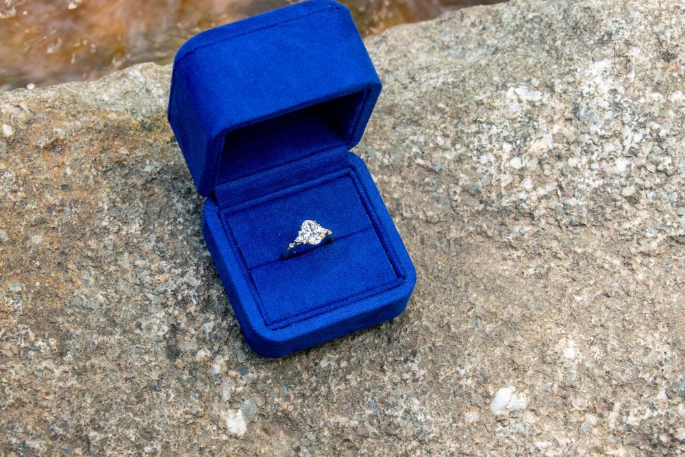 Diamond solitaire engagement ring in open blue velvet ring box on stone surface.