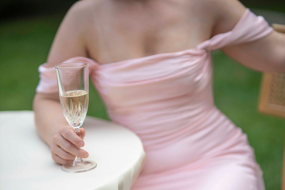 Someone in a pink off-shoulder dress holds a glass of champagne at an outdoor event.