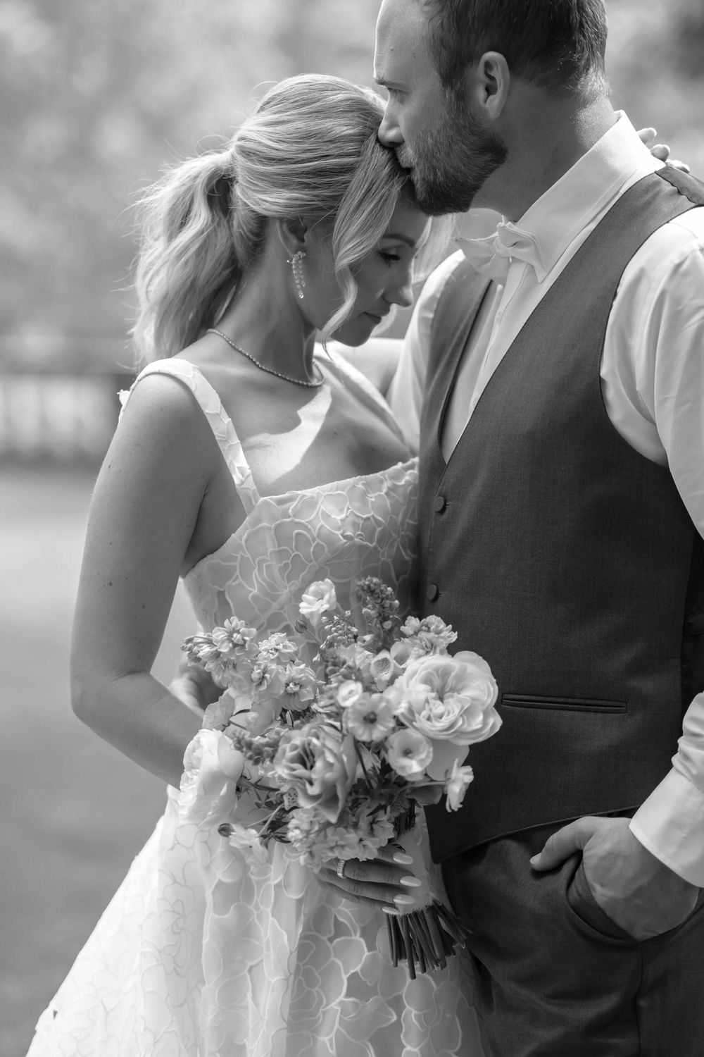 Black and white wedding photo showing tender moment between newlyweds as bride holds elegant floral bouquet.