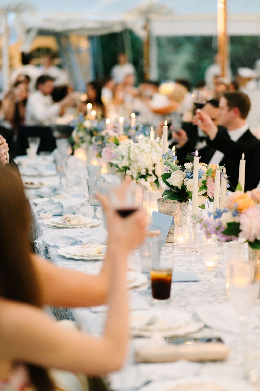 Elegant wedding reception table with floral centerpieces, candles, and guests raising glasses for a toast.