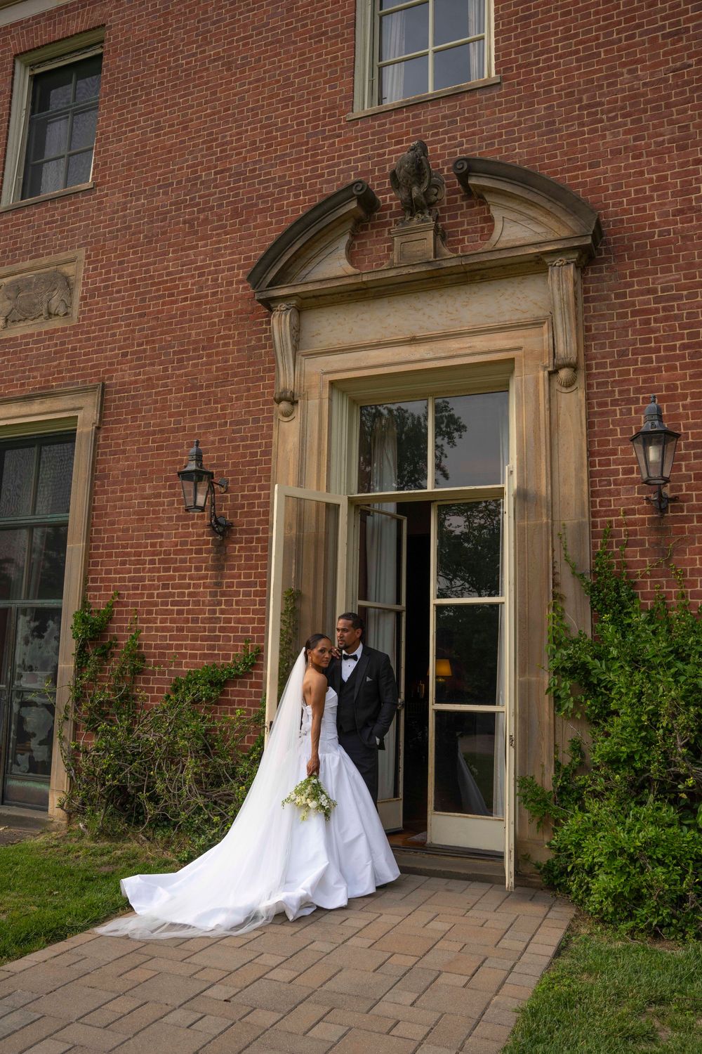 A newly married couple poses outside an elegant brick building entrance with ornate architectural details and lanterns.