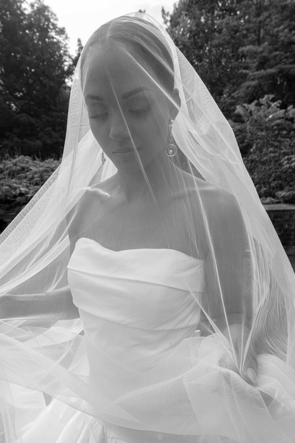 Elegant bridal portrait in black and white showing a serene pose with a flowing veil and strapless wedding gown.