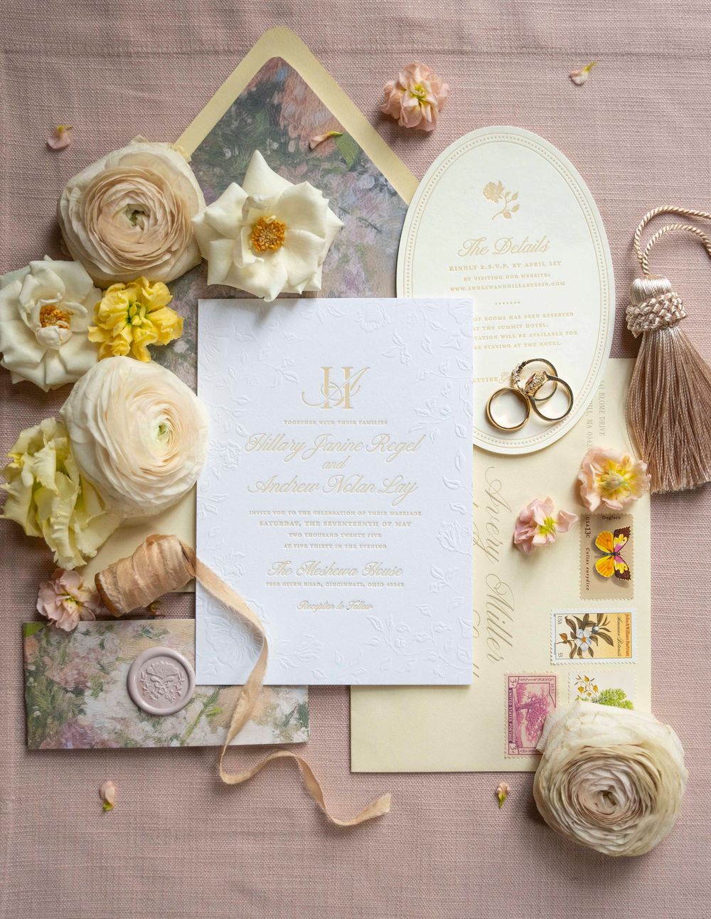 Elegant wedding invitation suite with white and gold letterpress design surrounded by soft pastel flowers and gold rings.