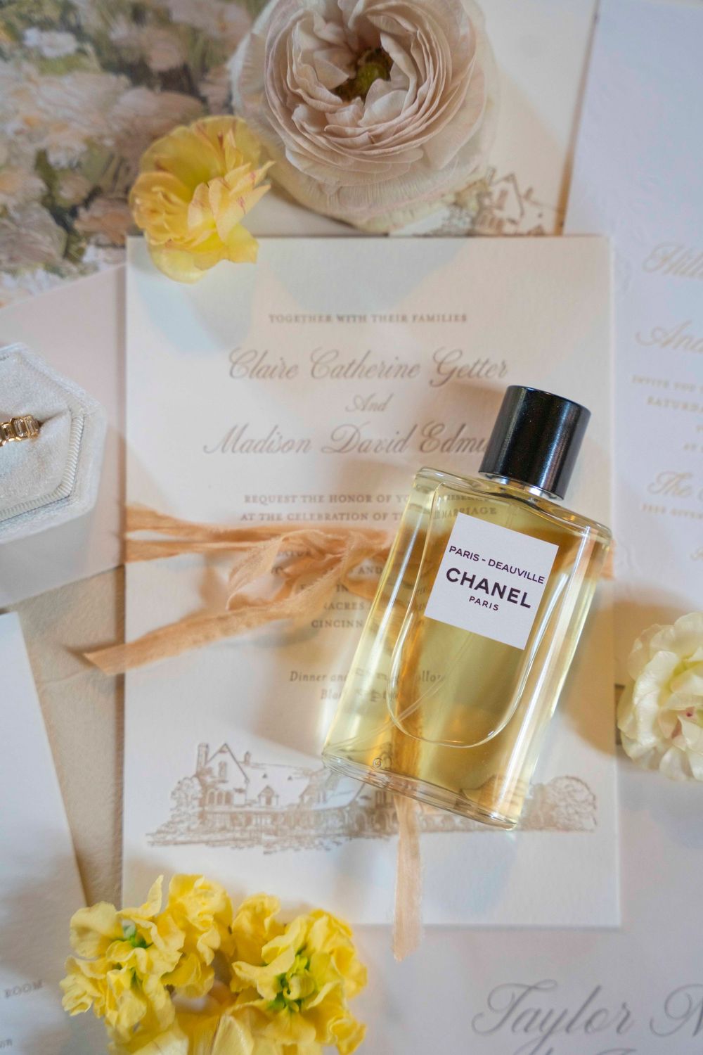Elegant wedding invitations displayed with Chanel perfume bottle and yellow flowers on white background.