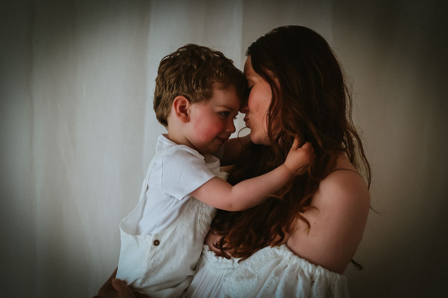 Intimate moment between mother and child in white clothing against dark background.