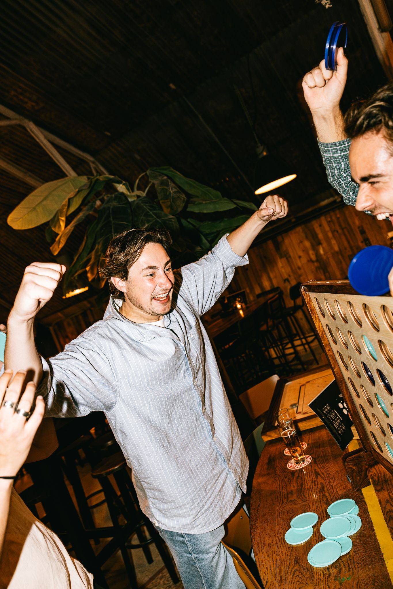 Excited young people celebrating victory while playing beer pong at a bar with wooden decor.