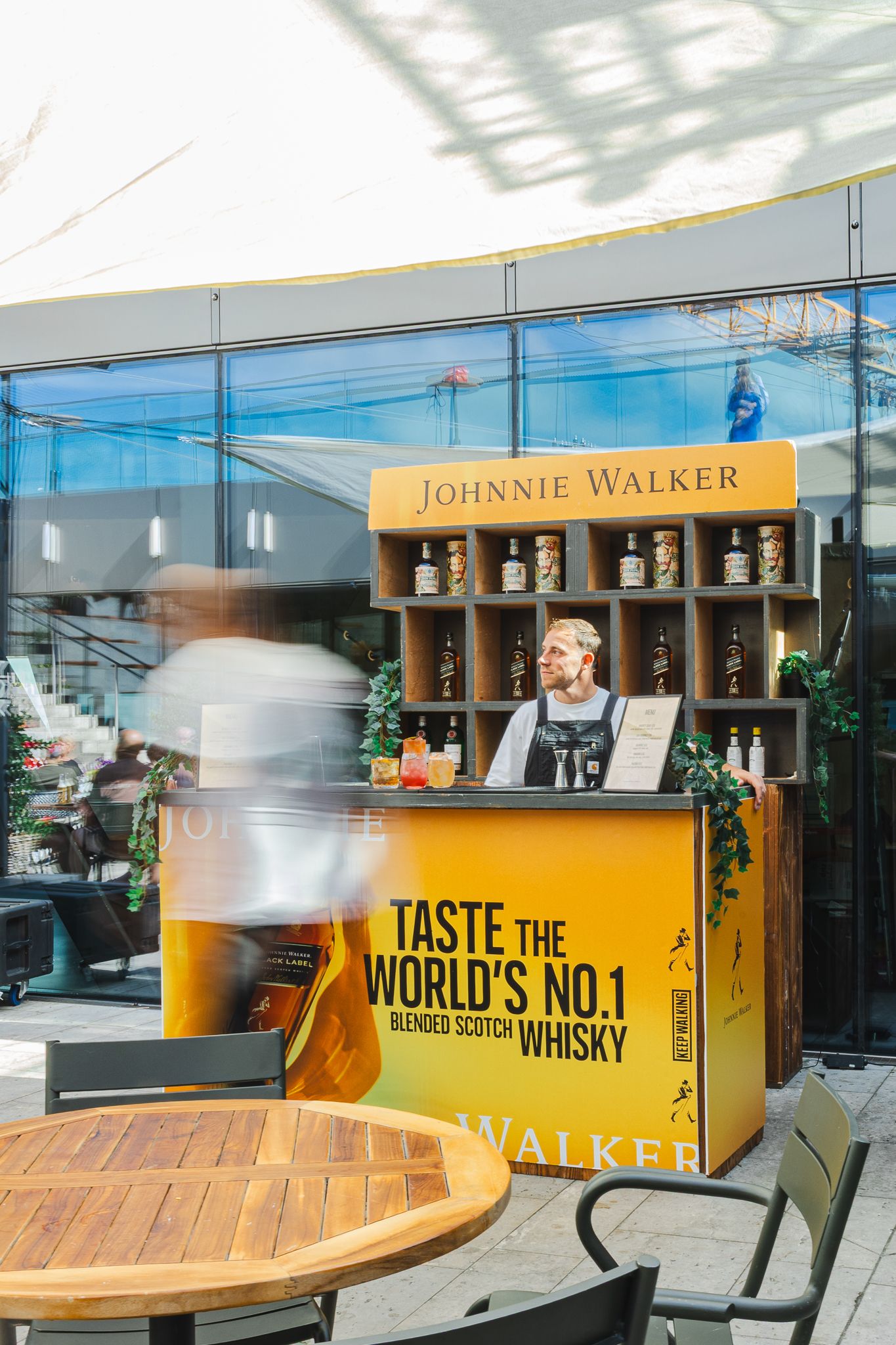 A Johnnie Walker promotional bar display with wooden shelving and bottles at an outdoor patio setting.