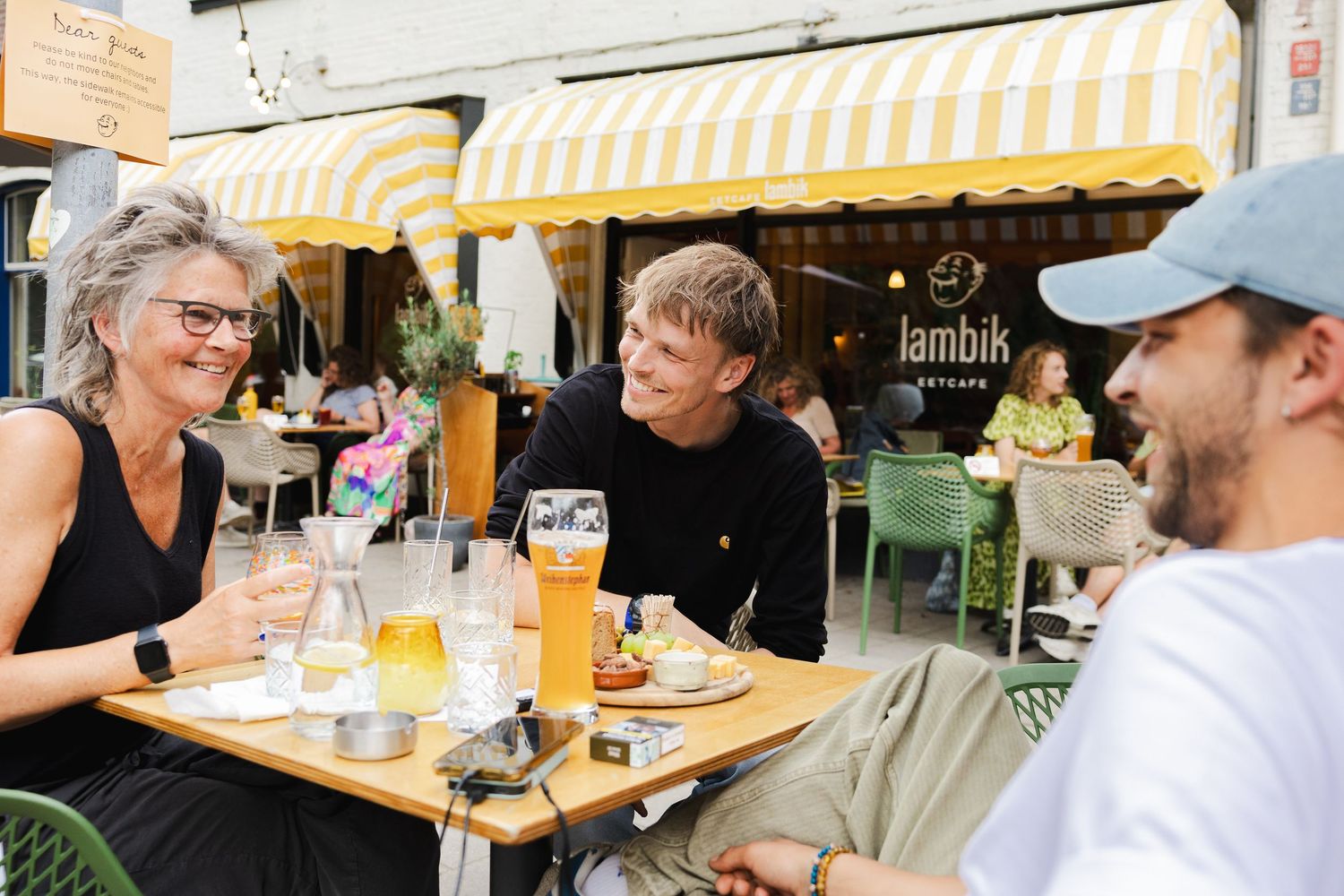 Restaurant patrons enjoy outdoor dining at a vibrant patio with yellow awnings and wooden tables on a sunny day.