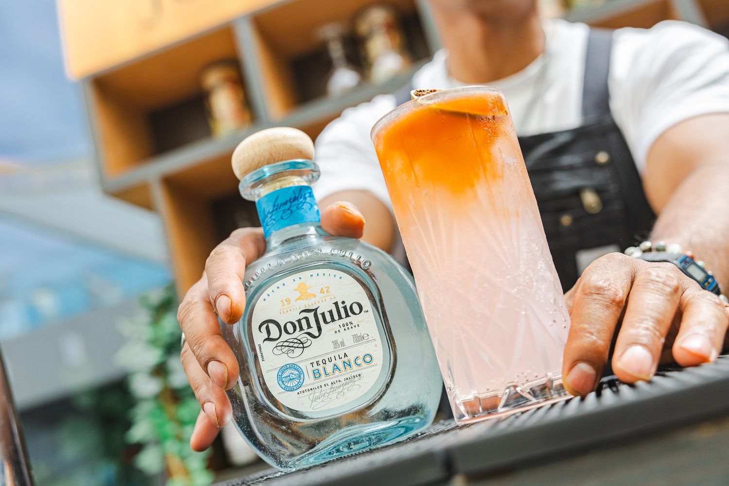A glass of pink ombre cocktail sits next to a bottle of Don Julio tequila on a serving tray.