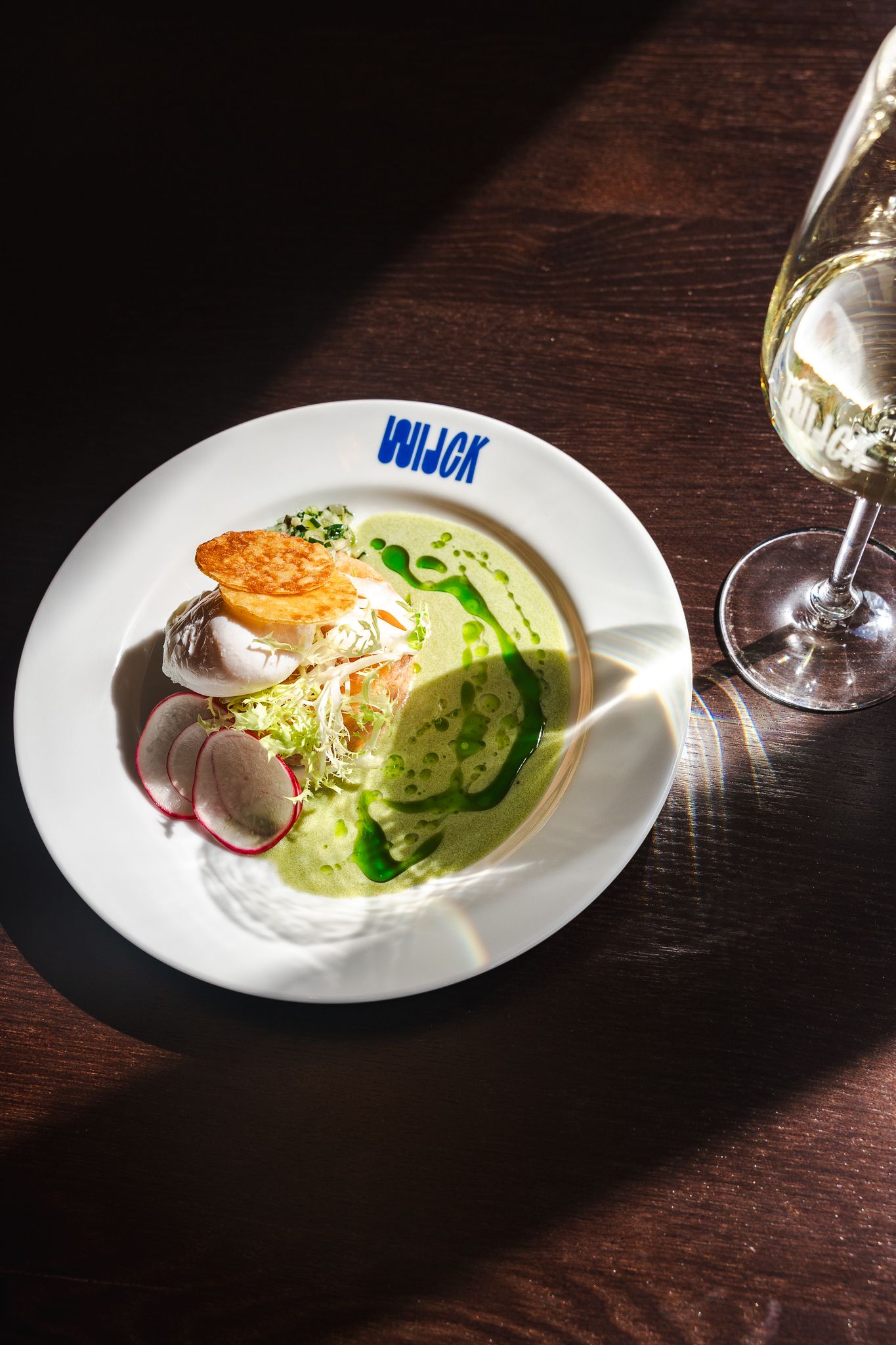 A white plate with sliced cucumbers and garnish served on a dark wooden table in moody restaurant lighting.