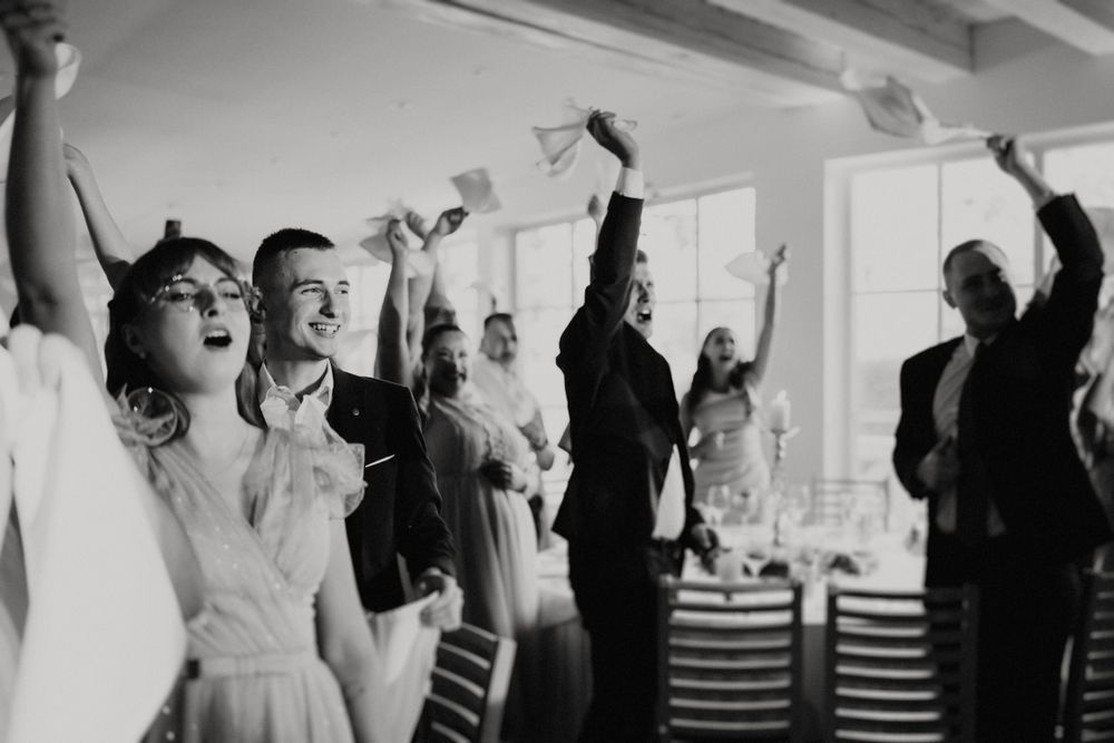 Joyful celebration with guests raising their arms in a black and white photo.