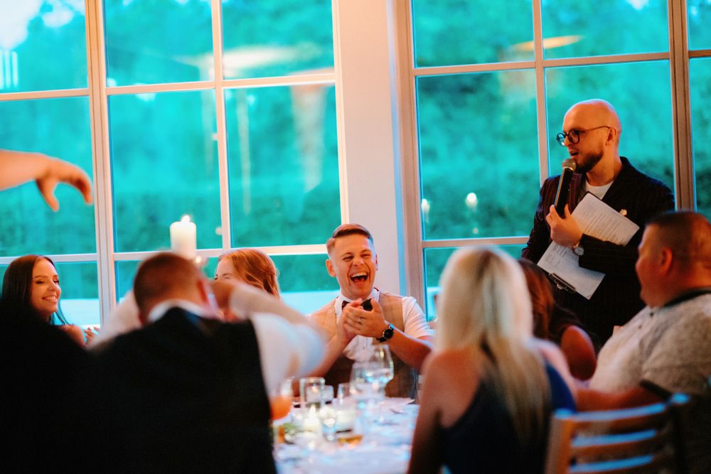 Wedding reception venue with large windows and turquoise lighting as guests celebrate at decorated tables.