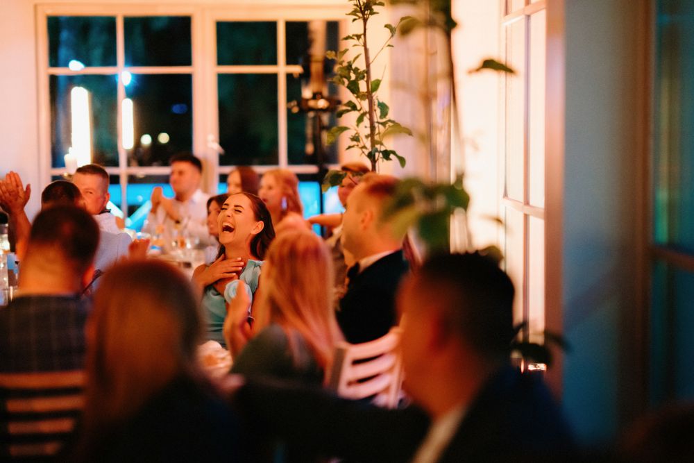 Warm-lit wedding venue with large windows showing guests celebrating during golden hour.