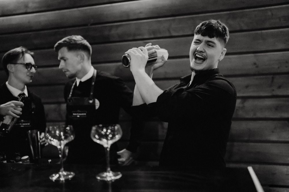 Black and white photo of guests socializing and toasting at an intimate reception gathering.