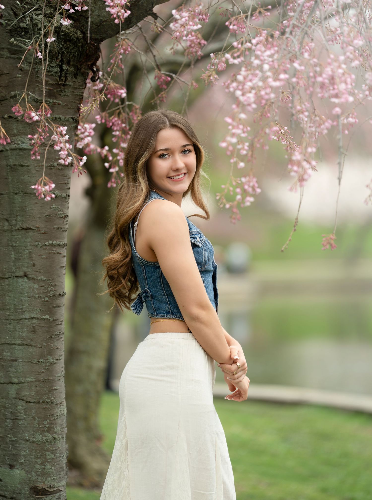 A smiling person in a denim crop top and white skirt poses by blooming cherry blossom trees in springtime.Cleveland,Ohio