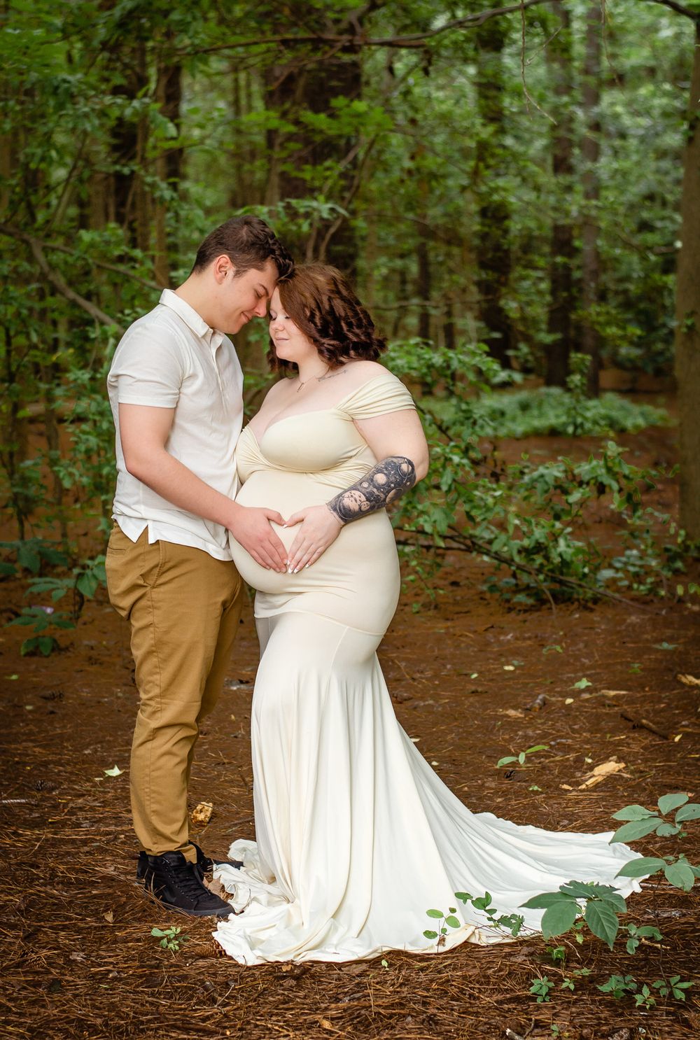 A loving maternity portrait of a couple in an intimate pose against a wooded background.