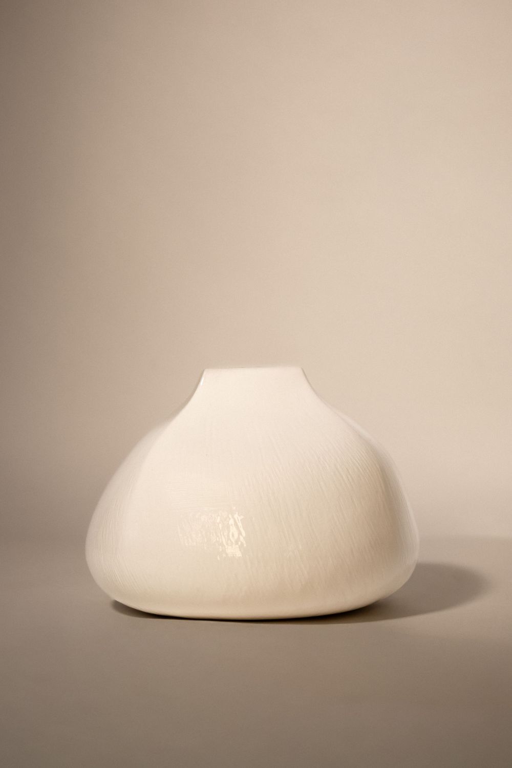 White ceramic vase with organic rounded shape and glossy crackle glaze finish, photographed on neutral beige background.